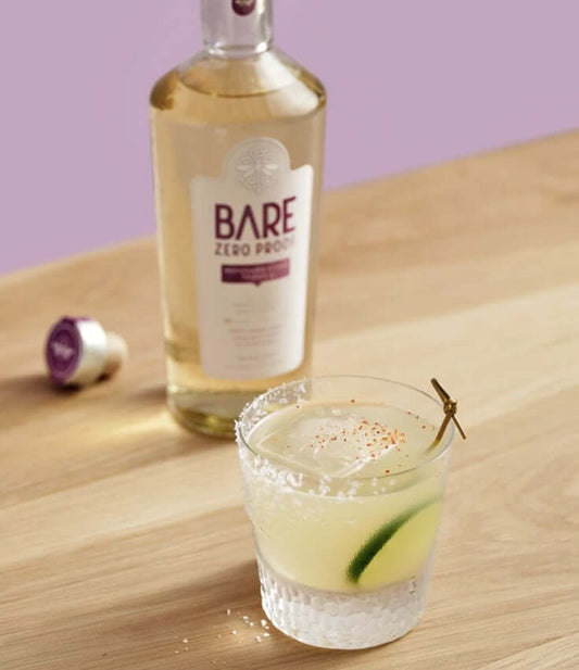 Bottle of BARE ZERO PROOF® Reposado Style Tequila and a BARE Desnudo Zero-Proof Margarita on a table.