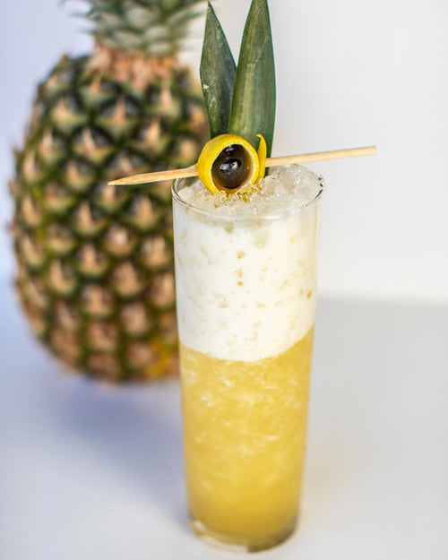 A Piña BARELADA Zero-Proof Piña Colada alternative cocktail in a glass in front of a pineapple, made with BARE ZERO PROOF® Rum Blanco